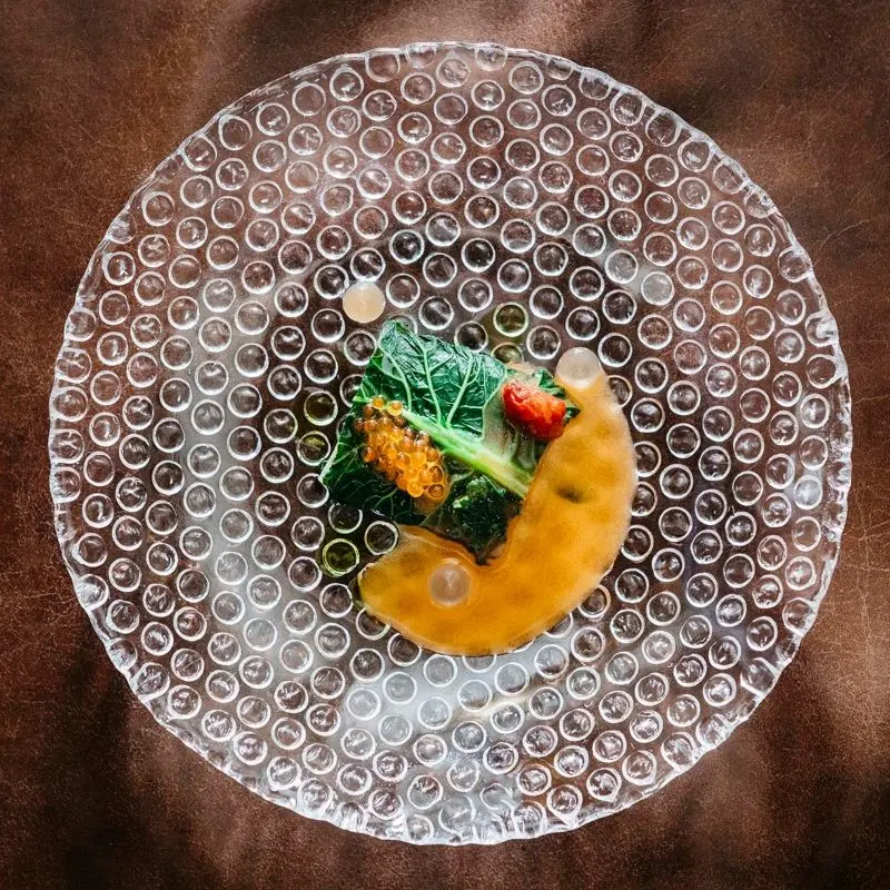 Detail fine dining pokrmu servírovaného na skleněném talíři s texturou bublin.